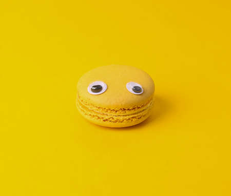 Minimal food concept. Yellow French macaroon with eyes on yellow backgroundの写真素材