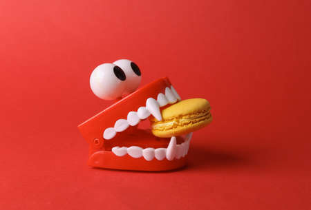 Toy jaw vampire with french macaroon in the teeth on red background. halloween conceptの写真素材