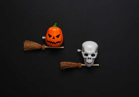Minimal halloween still life. Jack lantern and skull toy with witch's brooms on black background. top viewの写真素材