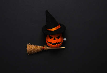 Minimal halloween still life. Jack lantern toy with witch's broom and hat on black background. top viewの写真素材