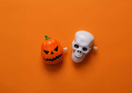 Minimal halloween still life. Clockwork head of jack o'lantern and skeleton skull on orange background. top viewの写真素材