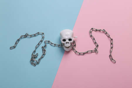 Minimal halloween still life. Clockwork skeleton skull with steel chain on blue pink background. top viewの写真素材