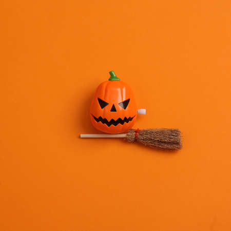 Minimal halloween still life. Jack lantern toy with witch's broom on orange background. top viewの写真素材