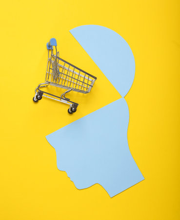 Open your mind, mental health concept, creative thinking. Paper silhouette of human head and shopping trolley on yellow backgroundの写真素材