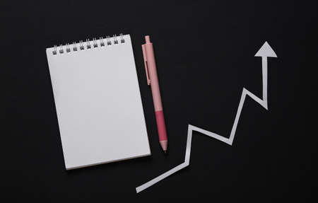 Analytics, statistics, business concept. Growth arrow with notepad on black background. top view