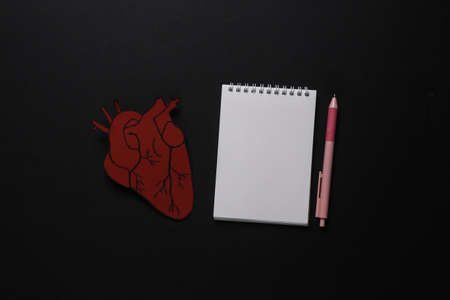 Diagnosis of heart disease. Anatomical heart with notebook on black background