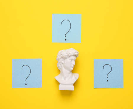 Memo pieces of paper with question marks and David bust on yellow background. Business, psychology, answers to questions conceptの写真素材