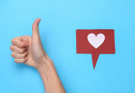 Female hand showing thumbs up gesture with like notification icon on blue background. social media. Rating, followers feedbackの写真素材