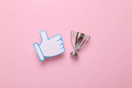 Thumbs up notification icon with winner cup on pink background. competition. social media. Rating, followers feedbackの写真素材