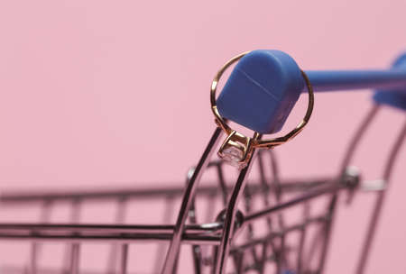 Shopping trolley with diamond ring on a pink background. Marriage proposal conceptの写真素材