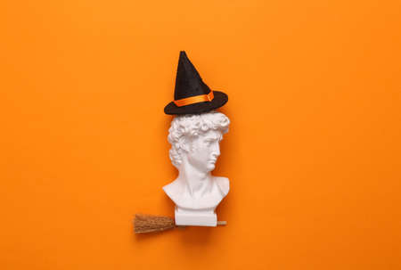 David bust on a witch's broom with hat on orange background. October 31st, happy halloween concept, minimal layout. top viewの写真素材