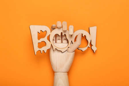 Minimal halloween layout. Wooden hand holding word boo! on orange background. Trick or treat. top viewの写真素材
