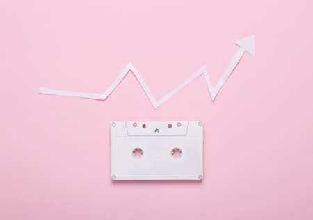 Audio cassette with growth arrow on pink background. Music listening statistics