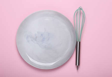 Empty ceramic plate with whisk on pink background. top viewの写真素材