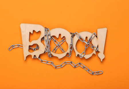 Happy halloween concept. The word boo! wrapped with a steel chain on an orange backgroundの写真素材