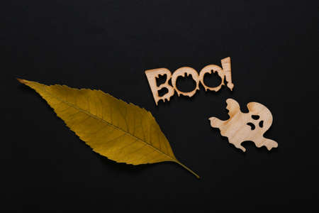 Happy halloween concept. Wood carved ghost and word boo! with autumn leaves on black background....