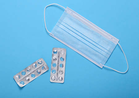 Blank blisters of pills with a facial mask on a blue background. Pandemic, quarantine, treatment...