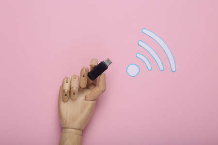 wifi icon and wooden hand holding usb flesh drive on pink background. top view