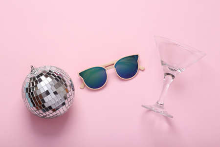 Minimal party concept. Sunglasses with a disco ball and cocktail glass on pink background. top viewの写真素材