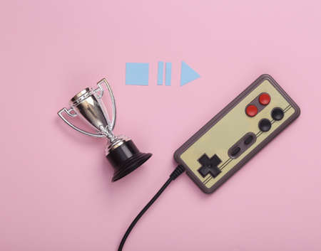 Winner cup with gamepad and icons start, stop, pause on pink background. Video game competition. top...