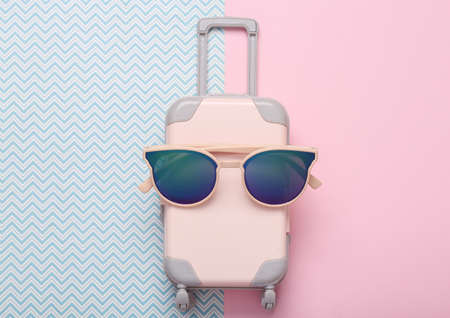 travel concept. toy luggage with sunglasses on blue pink background. top view. flat layの写真素材