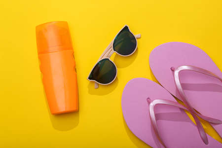 summertime. Resort, beach vacation concept. Sunglasses and a bottle of tanning cream, flip flops on yellow background. top viewの写真素材