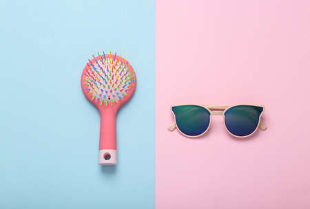 Women's accessories. Sunglasses with hairbrush on blue-pink background. top view