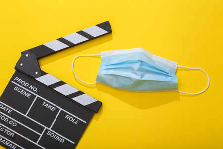 Movie clapperboard with medical mask on yellow background