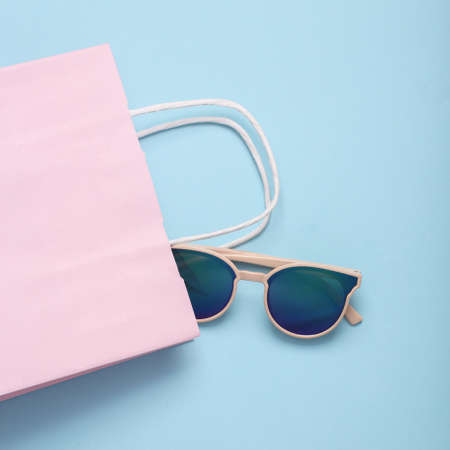 shopping concept. Paper shopping bag with sunglasses on blue pastel background. flat layの写真素材