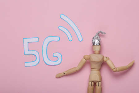 conspiracy theory. Wooden puppet in foil hat and word 5G on pink backgroundの写真素材