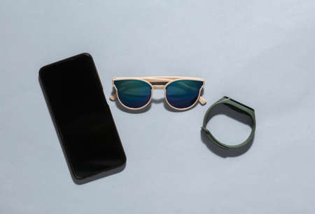 Modern gadgets on a gray background. Smartphone and smart bracelet with sunglasses on gray backgroundの写真素材