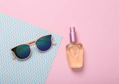 Women's accessories. Sunglasses with a bottle of perfume on a blue-pink pastel background. top viewの写真素材