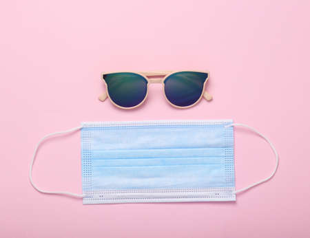 Medical mask with sunglasses on a pink background. creative still life. top viewの写真素材
