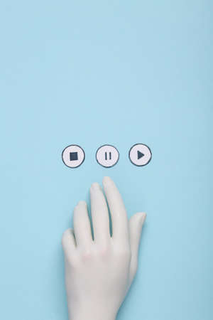Plastic hand chooses between icons start, stop, pause of media player on blue background.