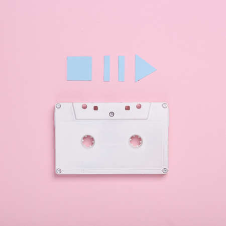 Audio cassette with icons start, stop, pause of media player on pink background. top view