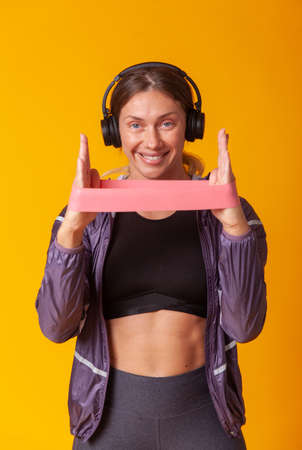 Portrait of a smiling athletic woman in headphones with a fitness band on a yellow background. healthy lifestyle. Aerobics and fitnessの写真素材