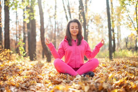 Young fit woman in pink sportswear meditates in the autumn forest. Yoga, spiritual harmonyの写真素材