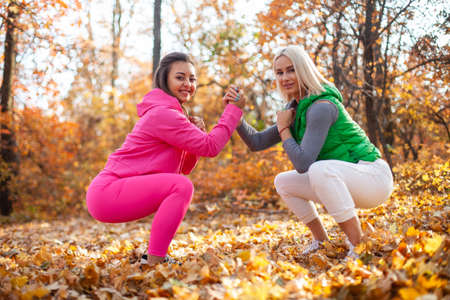 Active lifestyle concept. outdoor workout. Squat, holding hands. Two cute fit women are training...