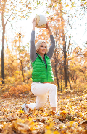 Beautiful active blonde woman training with medicine ball in autumn forest. Workout outdoor conceptの写真素材