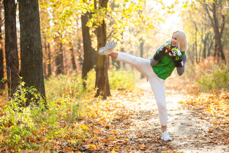Young smiling fit woman training kicks in boxing gloves in autumn forestの写真素材