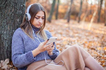 Pretty woman listening to music with stereo headphones in autumn forestの写真素材
