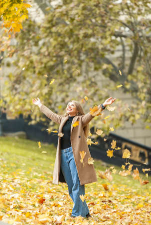 Young happy woman tossing fallen leaves in autumn parkの写真素材