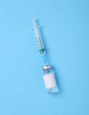 Vaccine bottle with a blank label for the brand and syringe on blue background. Covid 19 vaccination