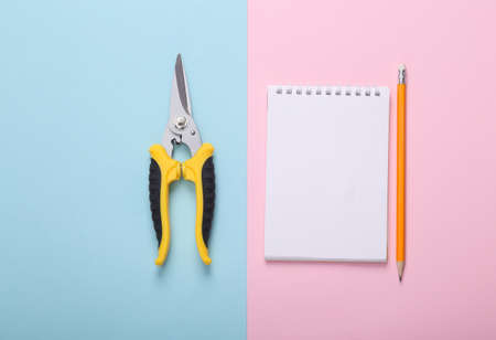 Garden pruner with notebook on pink blue background. top view