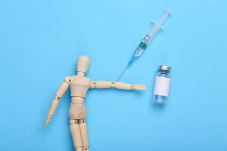 Wooden puppet makes a vaccine on a blue background.の写真素材