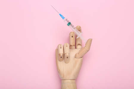 Wooden hand holds syringe on pink background. vaccinationの写真素材