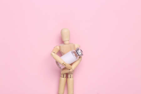 Wooden Puppet holding bottle vaccine on pink backgroundの写真素材