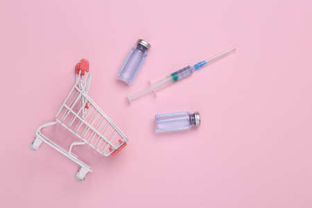 Shopping trolley with Vaccine bottles and syringe on pink background. top view. medical conceptの写真素材