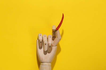 Wooden hand holding chili pepper on yellow background