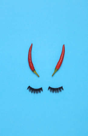Face made of eyelashes and chili peppers on a blue background. Halloween and beauty concept